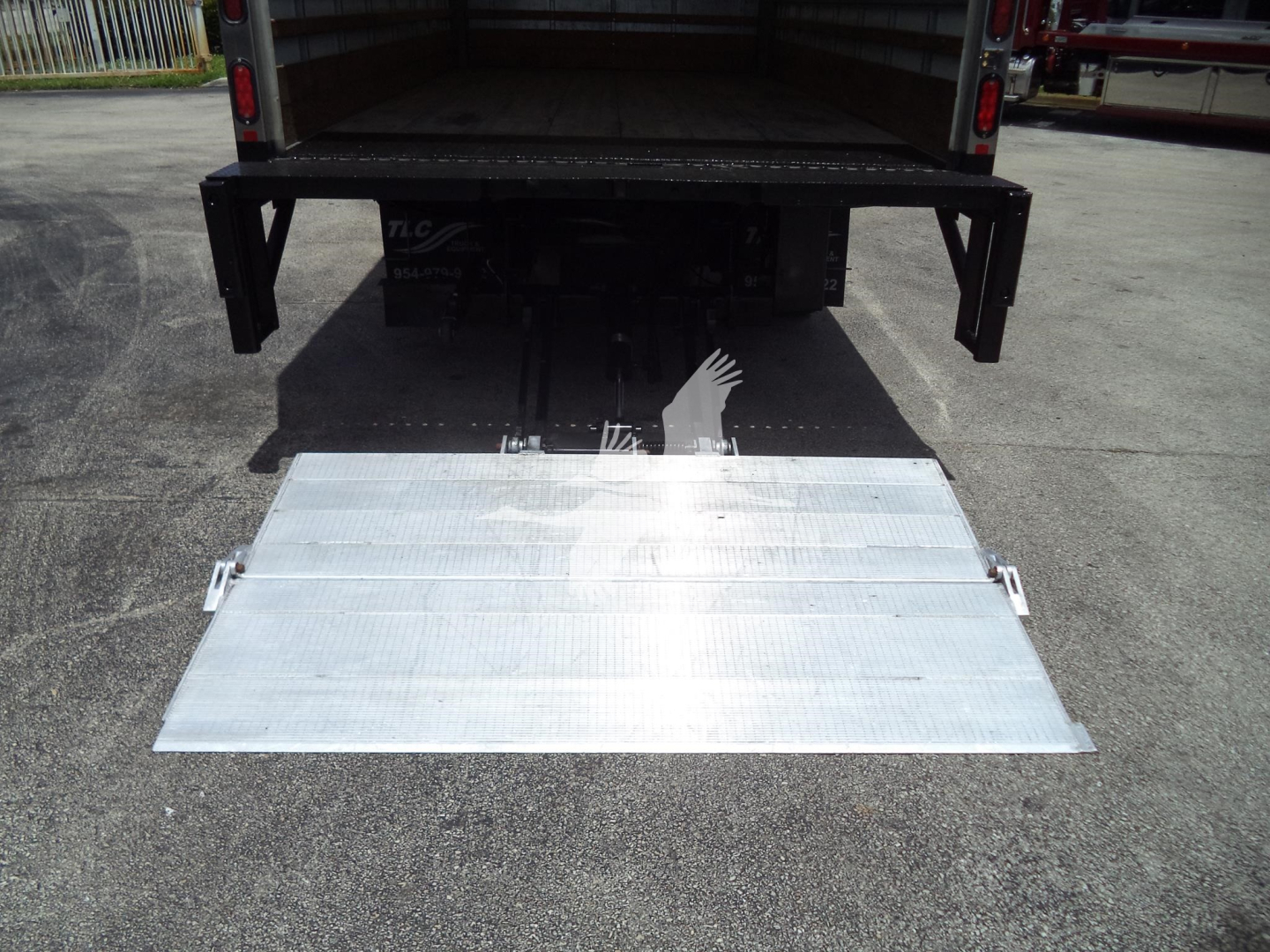 Isuzu NPR-HD truck with a lowered aluminum ramp at the back, showing the open cargo area and hydraulic mechanism under the platform.