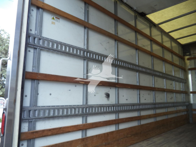 Vehicle interior cargo area showing metal sidewall with horizontal wooden battens and E-track rails. Light entering from open door.