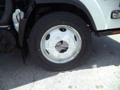 Isuzu NPR HD front wheel area showing tire, rim, and part of the front fender and lamp; visible markings on tire read 'NIT...' and some vehicle components like brake lines and reservoir.