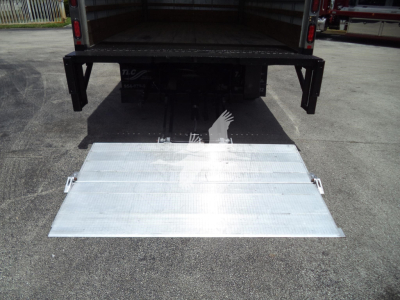 Isuzu NPR-HD truck with a lowered aluminum ramp at the back, showing the open cargo area and hydraulic mechanism under the platform.