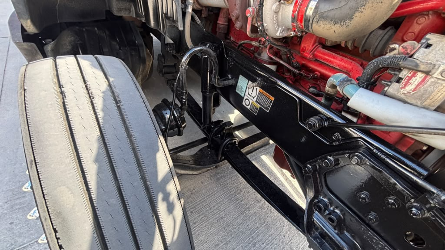Kenworth T680 engine bay view showing frame rails and suspension undercarriage with red engine components and black metal brackets.