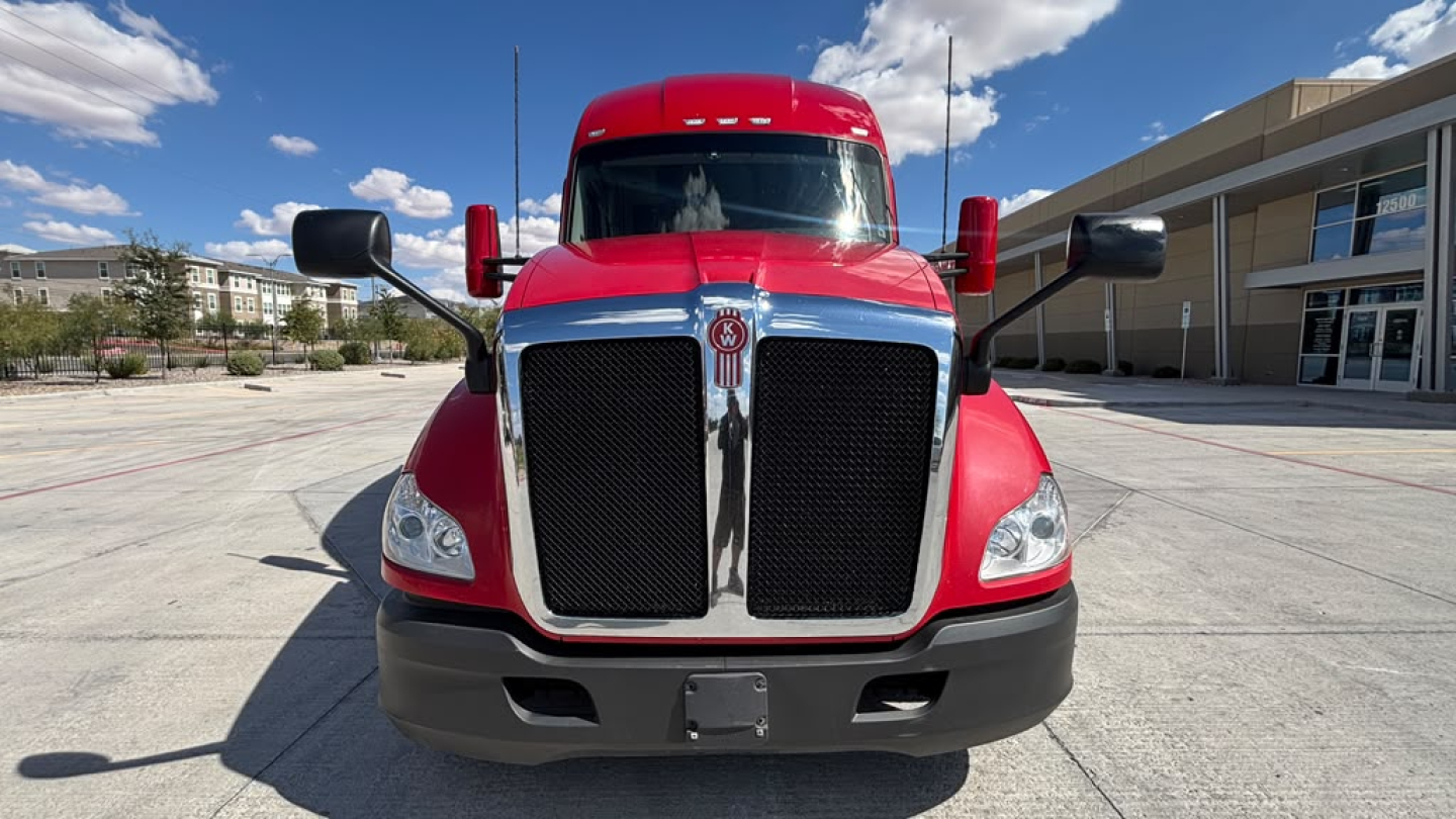 Kenworth T680 front view showing bold black grille, red cab, large side mirrors, and daylight in a dealership lot