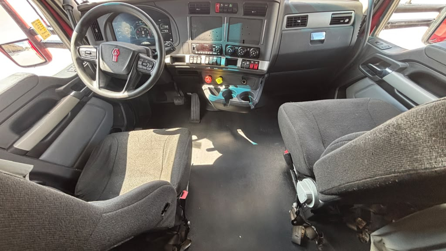 Kenworth T680 truck interior showing steering wheel, dashboard, center control cluster, driver and passenger seats, and floor pedals.