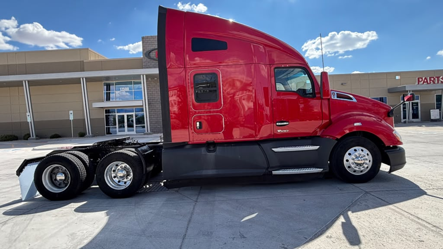 Kenworth T680 in-service truck side view showing red cab and black chassis with sleeper, dual rear axles, and wheels; clear sky above.