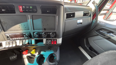 Trucking cab dashboard view showing ignition switches and gauges, with colored switches and knobs on center console and pedals visible.