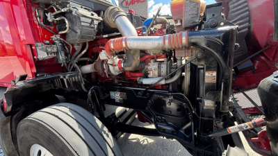 Kenworth T680 engine bay showing front suspension and diesel engine components with hoses and hoses clamps visible.