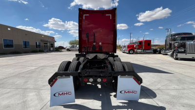 Rear view of a Kenworth truck chassis with red sleeper cab and MHC mud flaps, showing dual rear wheels and hitch area.