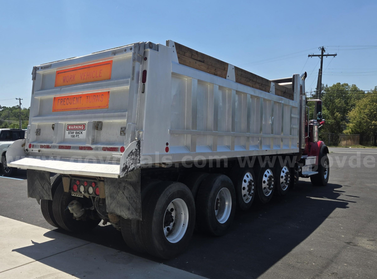 Dump truck showing rear and side of a white 2018 International HX with multiple axles and orange warning signs on tailgate.