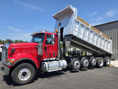 Dump truck with red cab and multi-axle dump bed in raised position.