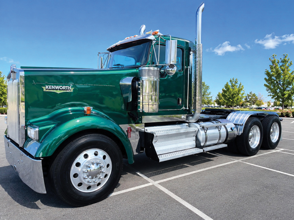 Kenworth W900L heavy-duty truck in green with chrome cab and dual rear axles, side view showing chrome exhaust stacks and fuel tanks.