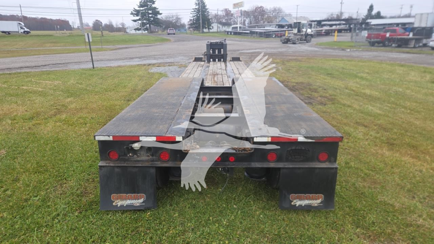 Lowboy trailer with flatbed sections, rear view showing black mud flaps and red brake lights, used condition.