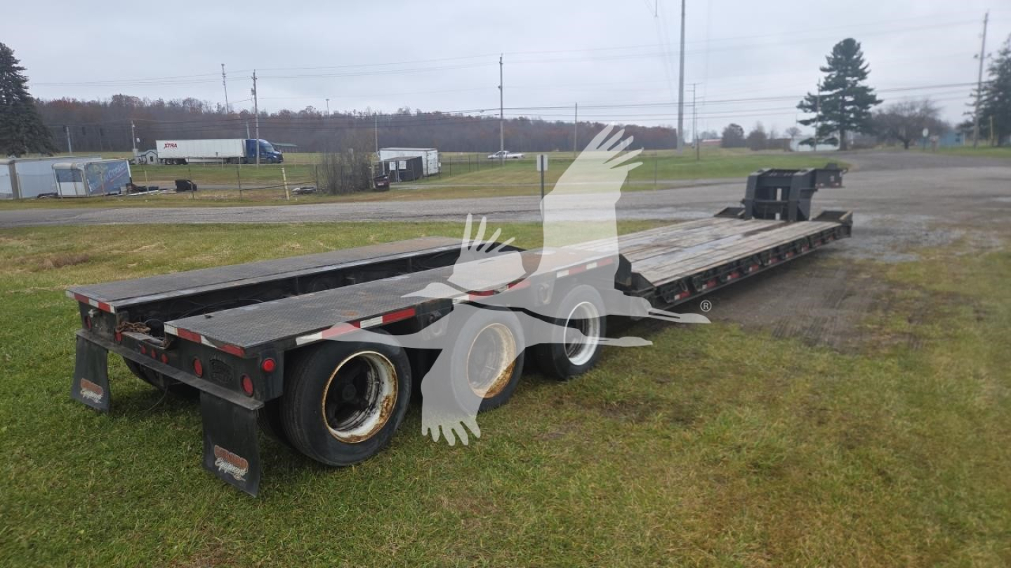 Ground bearing lowboy trailer showing dual rear axles and long flatbed with wheel wells and taillights.