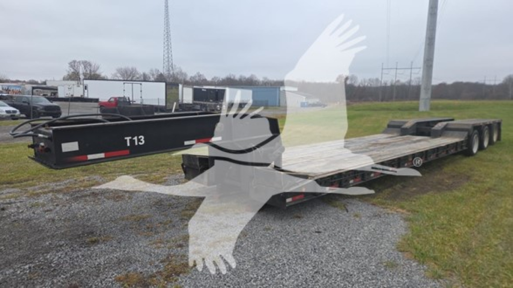 Lowboy trailer showing deck and triple-axle rear, Rogers T13 header, no cab in view, ground surface with gravel. Visible text: T13 on kingpin area and rear deck features.