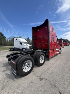 Red Freightliner Cascadia 126 semi tractor at a lot, rear view showing dual rear axles and fifth-wheel area.