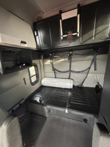 Interior sleeper cab of a 2022 Freightliner Cascadia 126 showing storage compartments, hanging net, and a mattress/bed area with a window to the side.