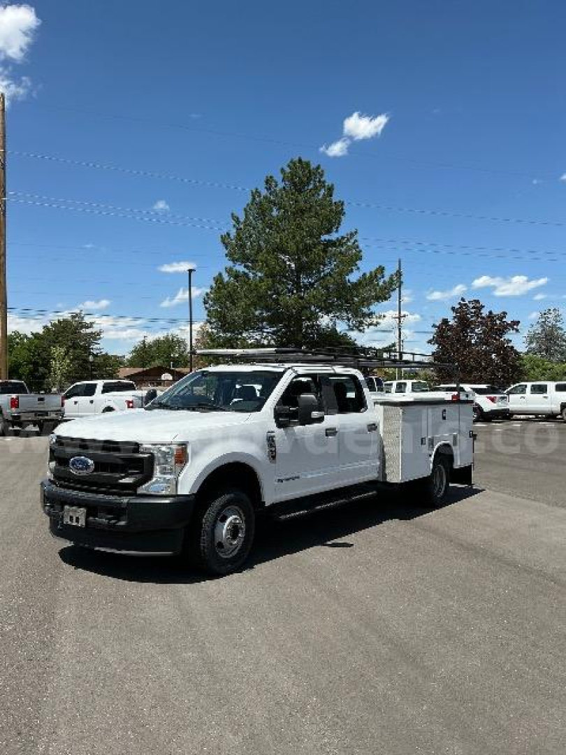 Ford F-350 utility/service truck in a dealership lot showing a white body, extended cab, utility bed with compartments, front grille and headlights visible.