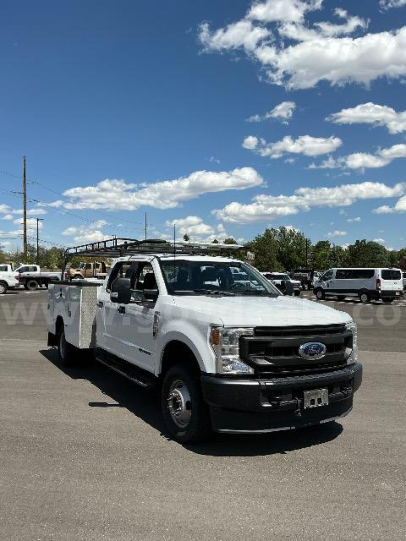 Ford F-350 utility truck in a parking lot, white dash with service body, front grille and bumper visible, clear sky
