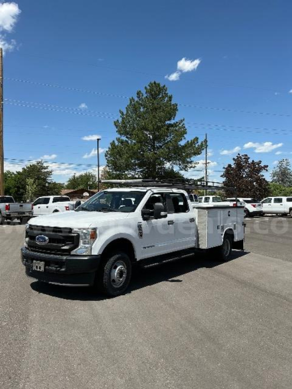 Ford F-350 utility/service truck in a dealership lot showing a white body, extended cab, utility bed with compartments, front grille and headlights visible.