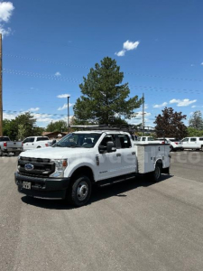 Ford F-350 utility/service truck in a dealership lot showing a white body, extended cab, utility bed with compartments, front grille and headlights visible.