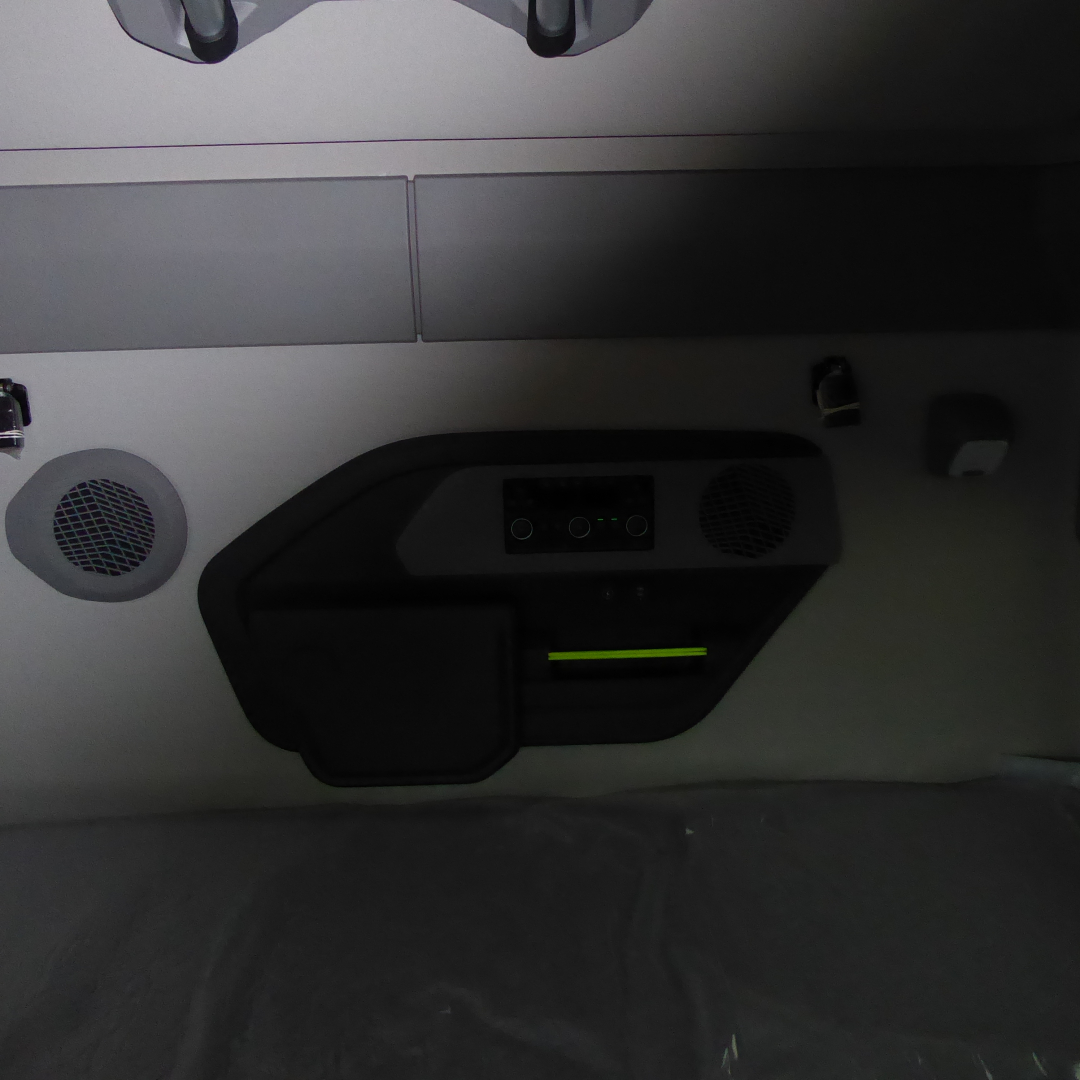 Cab interior of a Volvo VNL truck showing a control panel with a small screen, two circular speaker grills, and a glowing yellow-green horizontal line; overhead compartments and seating area visible.