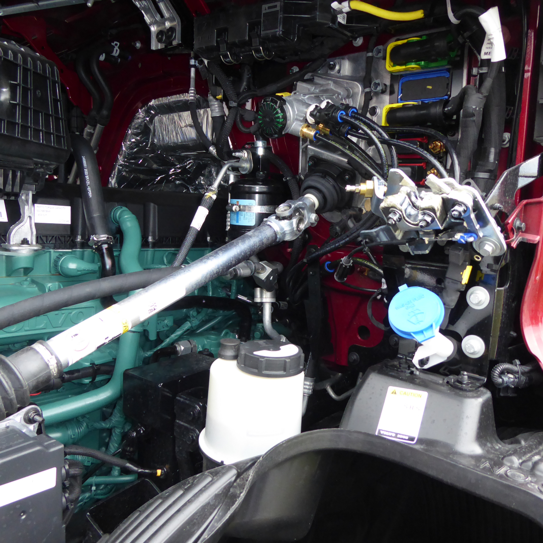 Volvo VNL64T860 engine bay view showing blue engine oil cap, green coolant reservoir, hydraulic lines, and wiring harnesses.