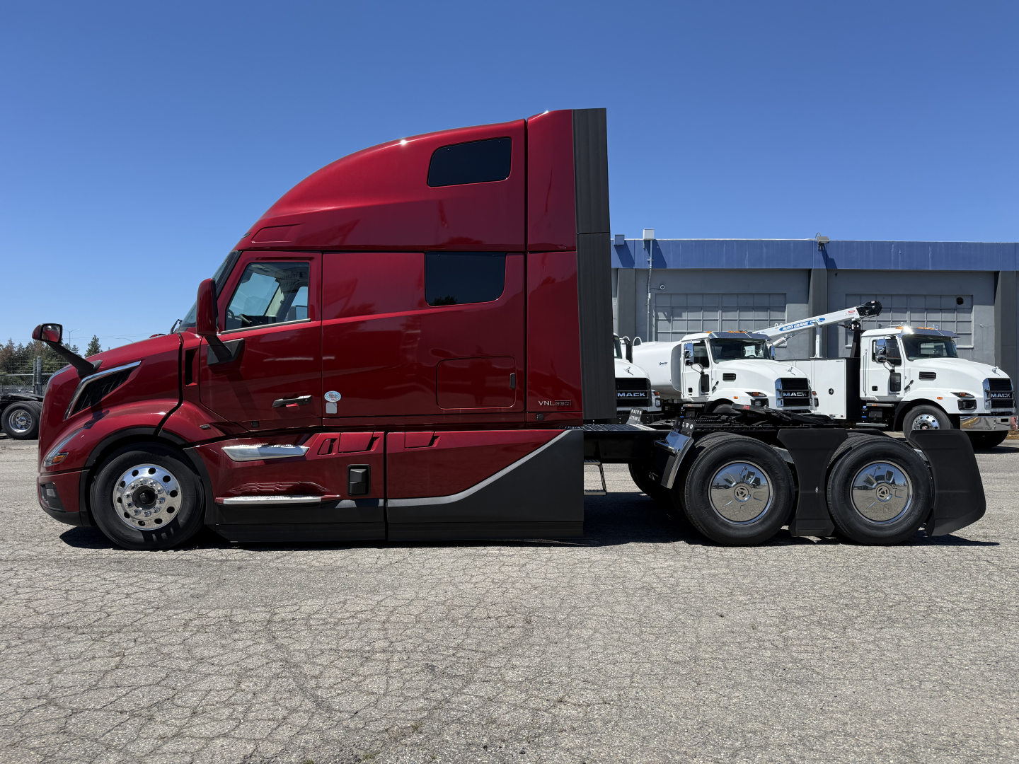 Volvo VNL64T860 tractor-trailer side view in red with sleeper cab, chrome wheels, and tow-ready rear wheels. No visible text on the truck exterior except reflections.
