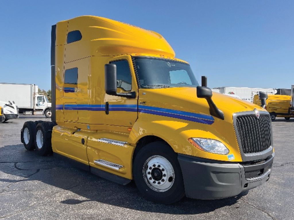 Truck cab in service showing bright yellow sleeper with blue stripe, International LT Series badge on grille, black bumper, side mirrors, and dual rear axles.