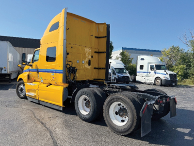 Truck tractor (yellow) in sleeper configuration with open rear, side view showing dual rear axles, black fifth wheel area, and vertical exhaust behind cab.