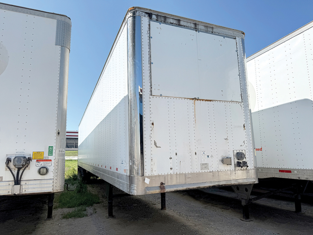 Reefer trailer in a yard showing rear and side panels with hinge door, aluminum finish, and support legs.