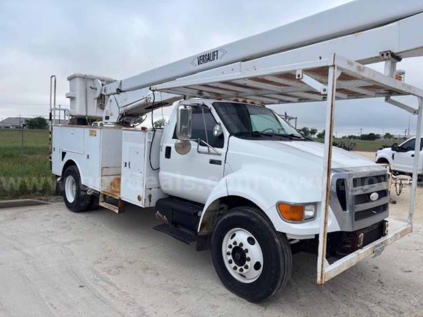 Ford F-750 bucket truck in-service showing hydraulic boom and Utility body with Versalift equipment label on the boom.