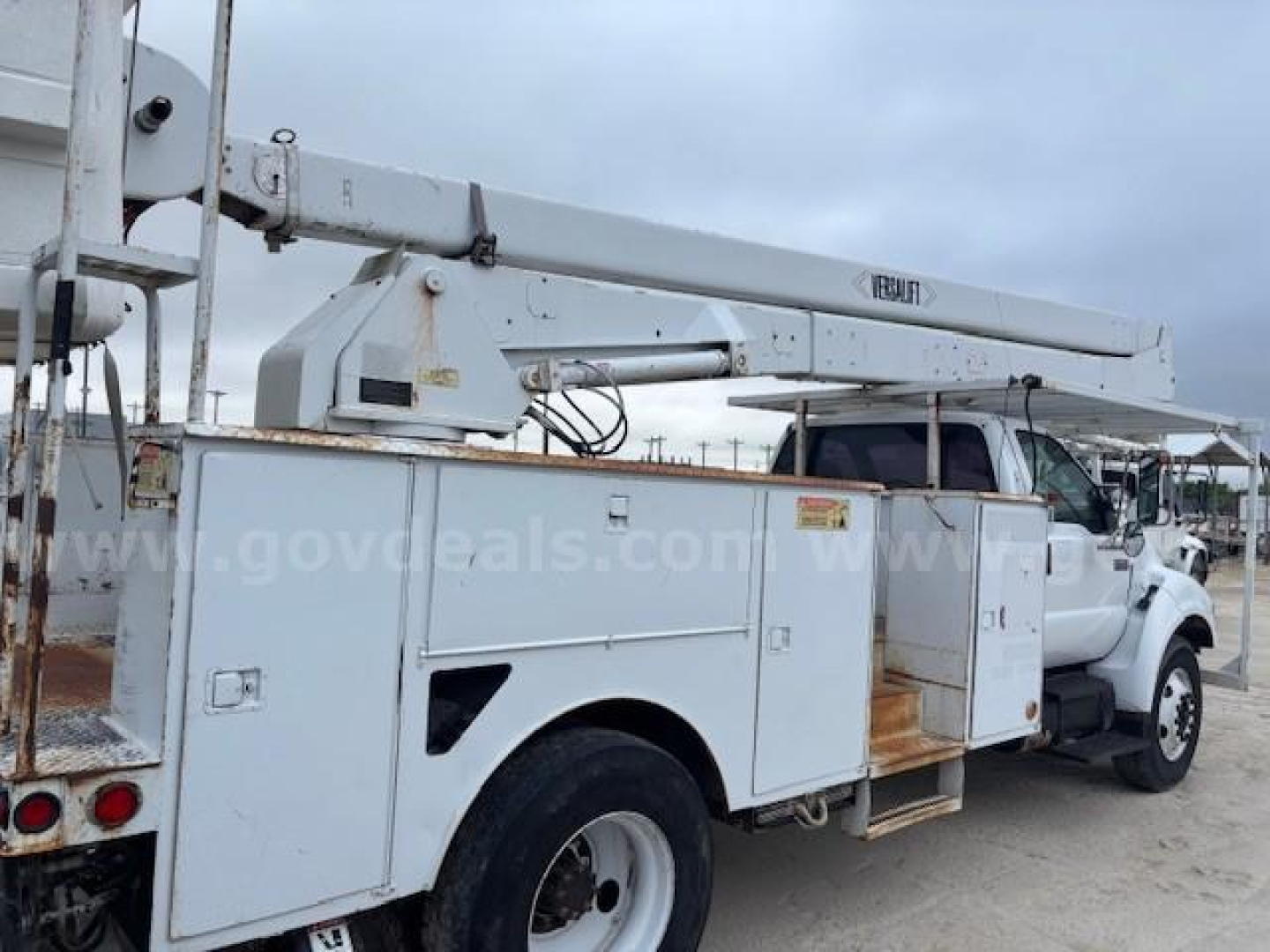 Service bucket truck with boom lift showing utility compartments and Ford bucket truck branding. Visible text includes 'FORD' on the boom arm and multiple utility compartments.
