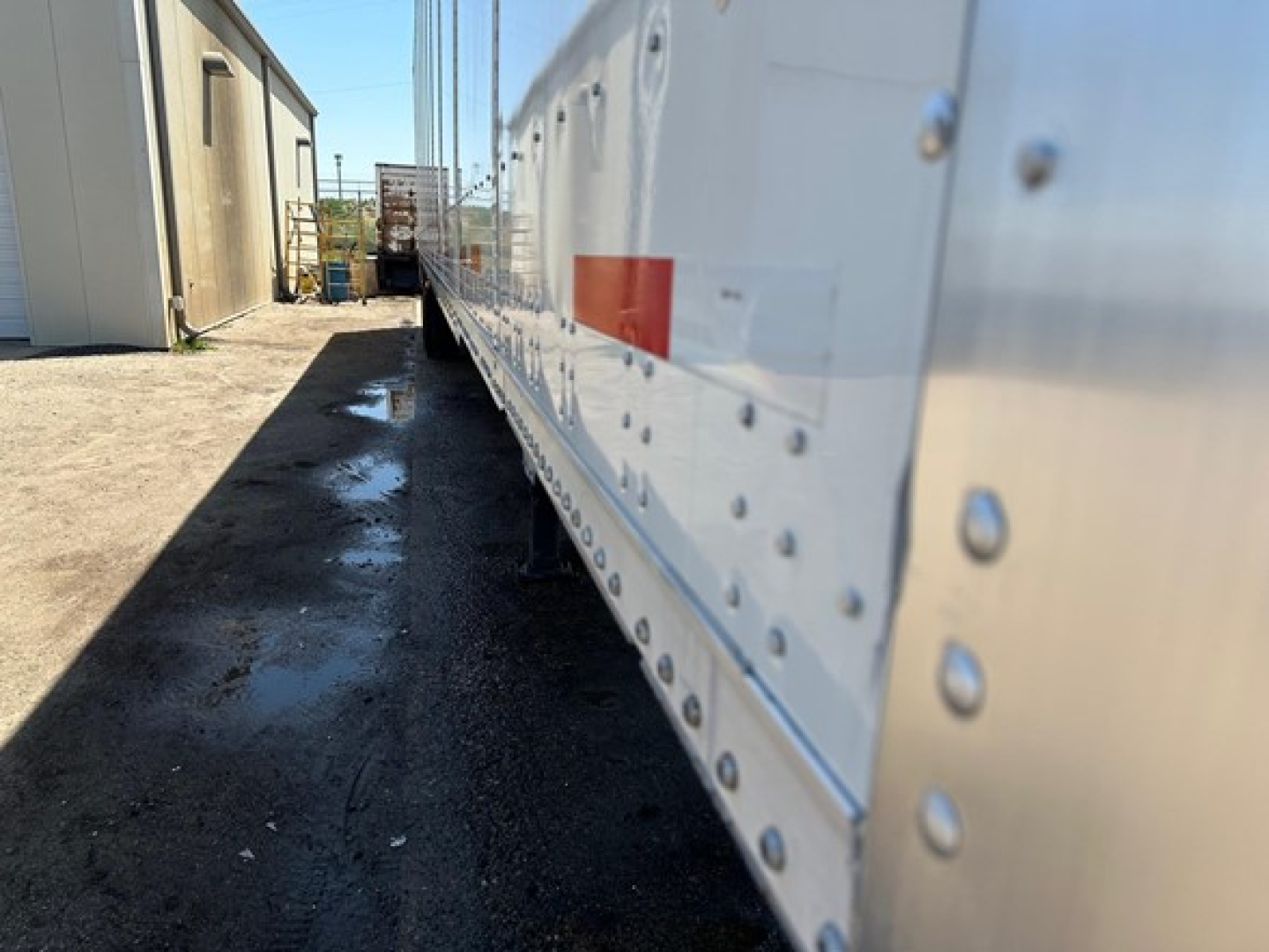 Side view of a white Wabash Duraplate dry van trailer with riveted aluminum panels, reflecting light, shop area in background.
