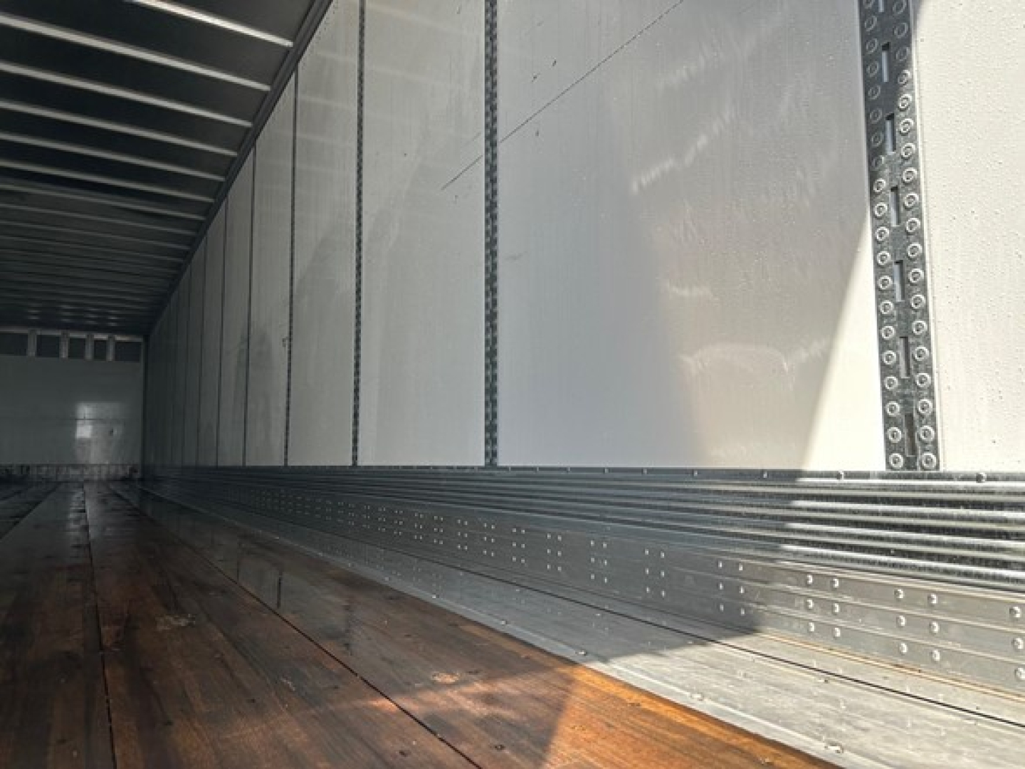 Trailer interior showing metal side walls and wooden floor with riveted channels and ledges.