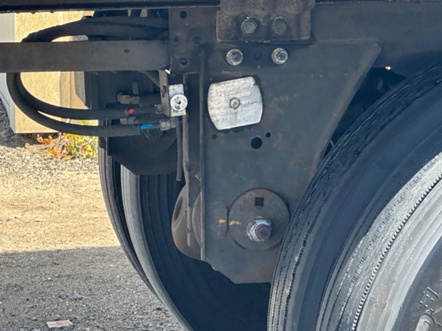 Trailer chassis and wheel area showing suspension mount, hoses, and a white rectangular placard with a circular bolt; part of a Wabash Duraplate dry van. 