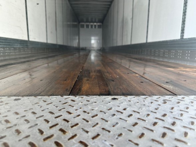 Interior of a Wabash dry van trailer with wooden floor and metal side walls; flicker of light at far end; diamond plate threshold. No visible text readable.
