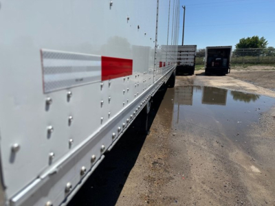 Trailer side of a white Wabash Duraplate dry van with riveted aluminum panels and red reflective tape, viewed from the side near a puddle.