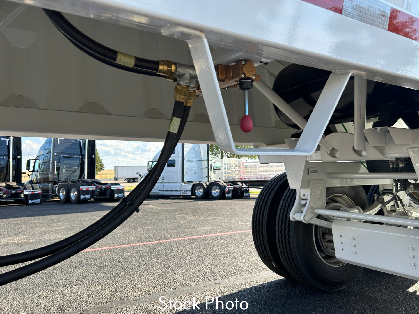 Trailer side view showing hydraulic hoses and wheel assembly; valve handles and undercarriage components visible.