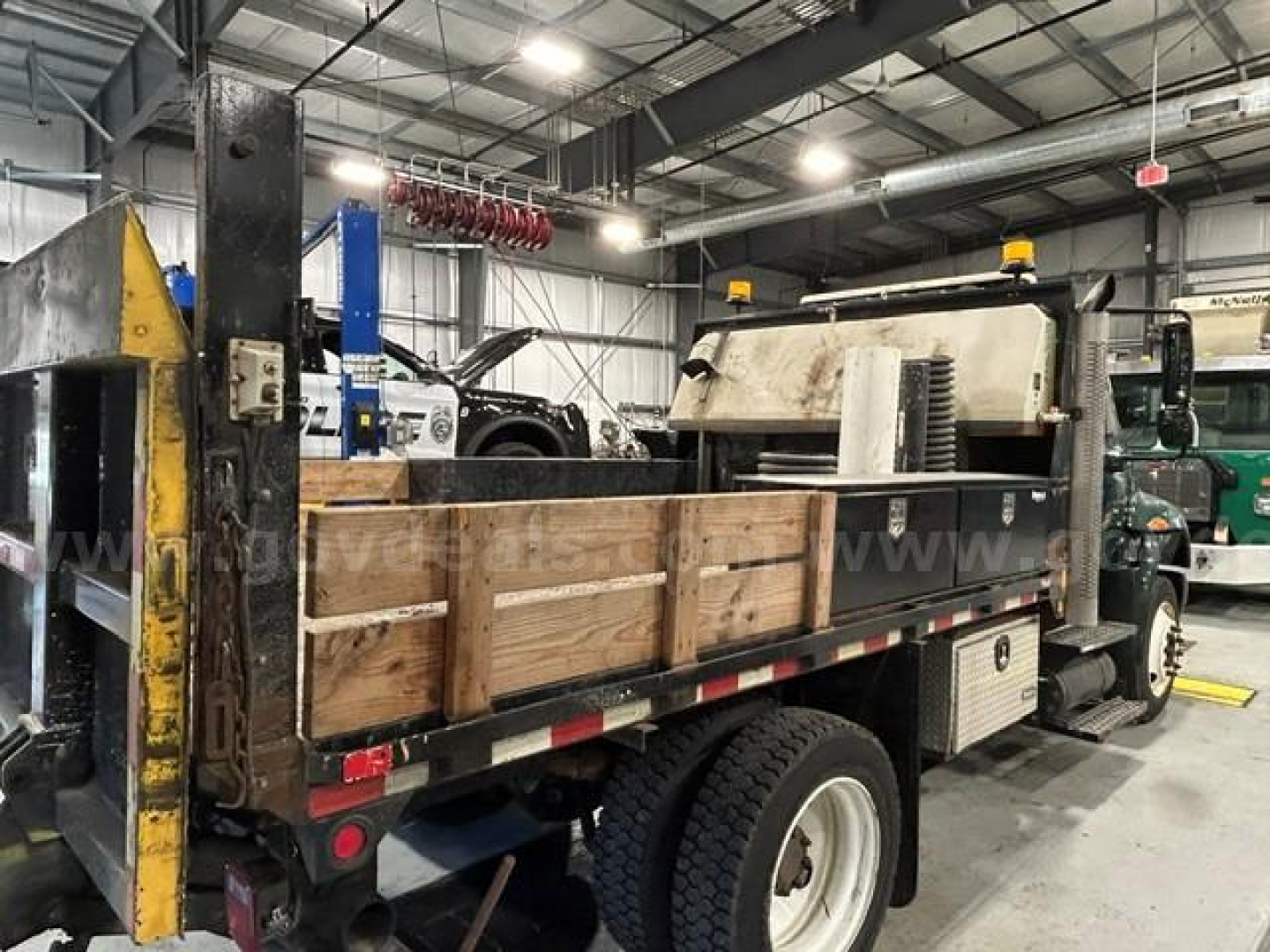 Service/utility truck bed with wooden side panels in an indoor shop; International 4300 rear view with crane equipment and yellow safety markers.