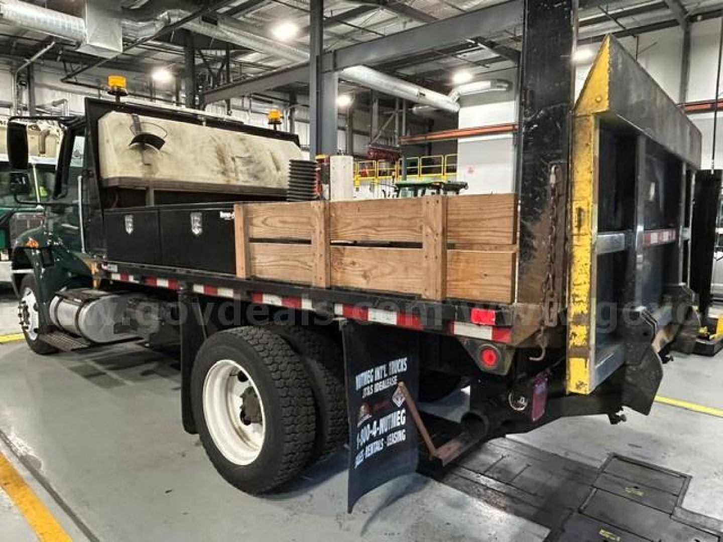 Service/utility truck bed on a 2011 International 4300 showing wooden side rails and black flatbed with tailgate in an indoor shop.