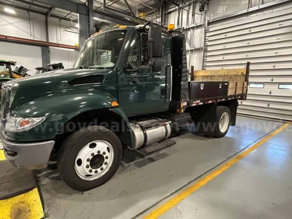 International 4300 medium-duty truck in service body with flatbed, dark green cab, inside industrial facility.