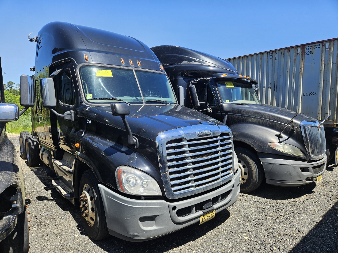 Freightliner Cascadia cab and chassis truck showing front view with chrome grille and blue cab, other truck in background.