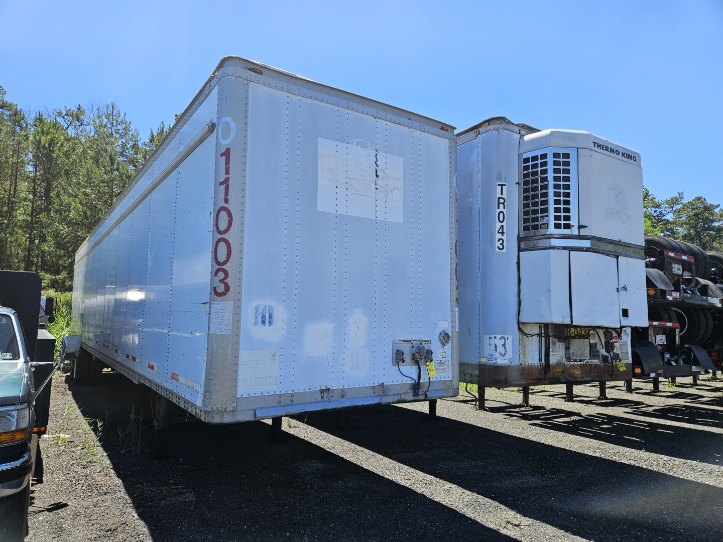 Freightliner Cascadia cab and chassis trailer unit in a salvage yard with a refrigerated truck trailer and a Thermo King unit visible.