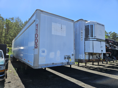 Freightliner Cascadia cab and chassis trailer unit in a salvage yard with a refrigerated truck trailer and a Thermo King unit visible.