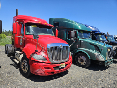 Red Freightliner Cascadia cab in view with other trucks in lot.