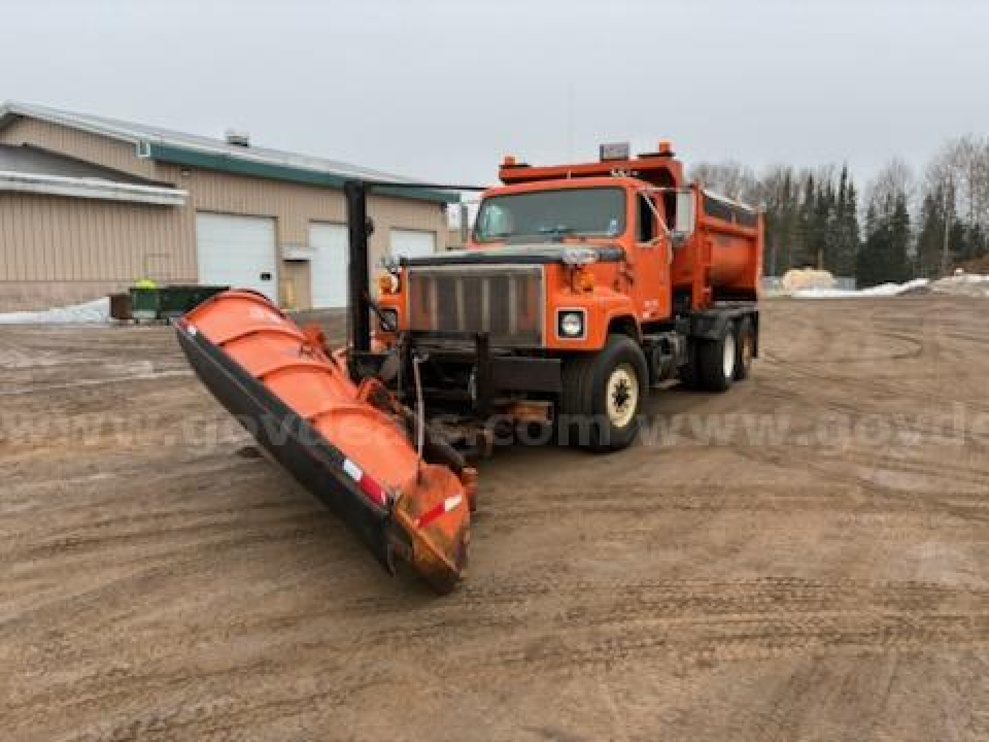 1997 International 2574 dump truck with large orange snow/ice plow attachment in front, parked on dirt lot near industrial buildings.