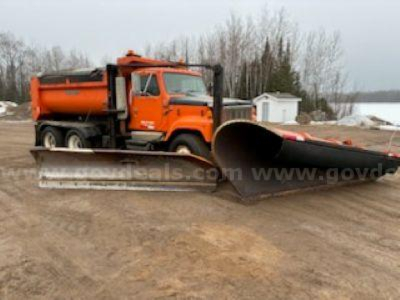 Dump truck with large orange snowplow blade attachment in foreground.