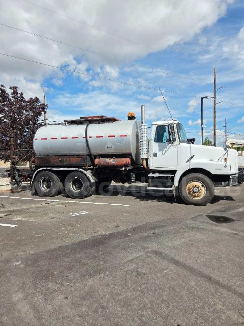 Truck side view showing a white Volvo S2000 vacuum/pressure tanker with large cylindrical tank and dual rear wheels.