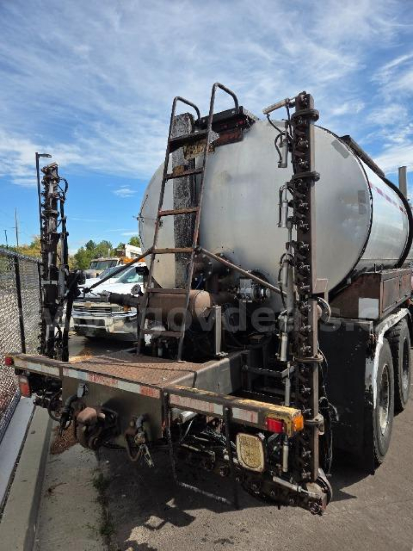 Rear of a tanker truck with a cylindrical tank, ladder racks, and hoses, viewed from the back left side.