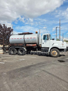 Truck side view showing a white Volvo S2000 vacuum/pressure tanker with large cylindrical tank and dual rear wheels.