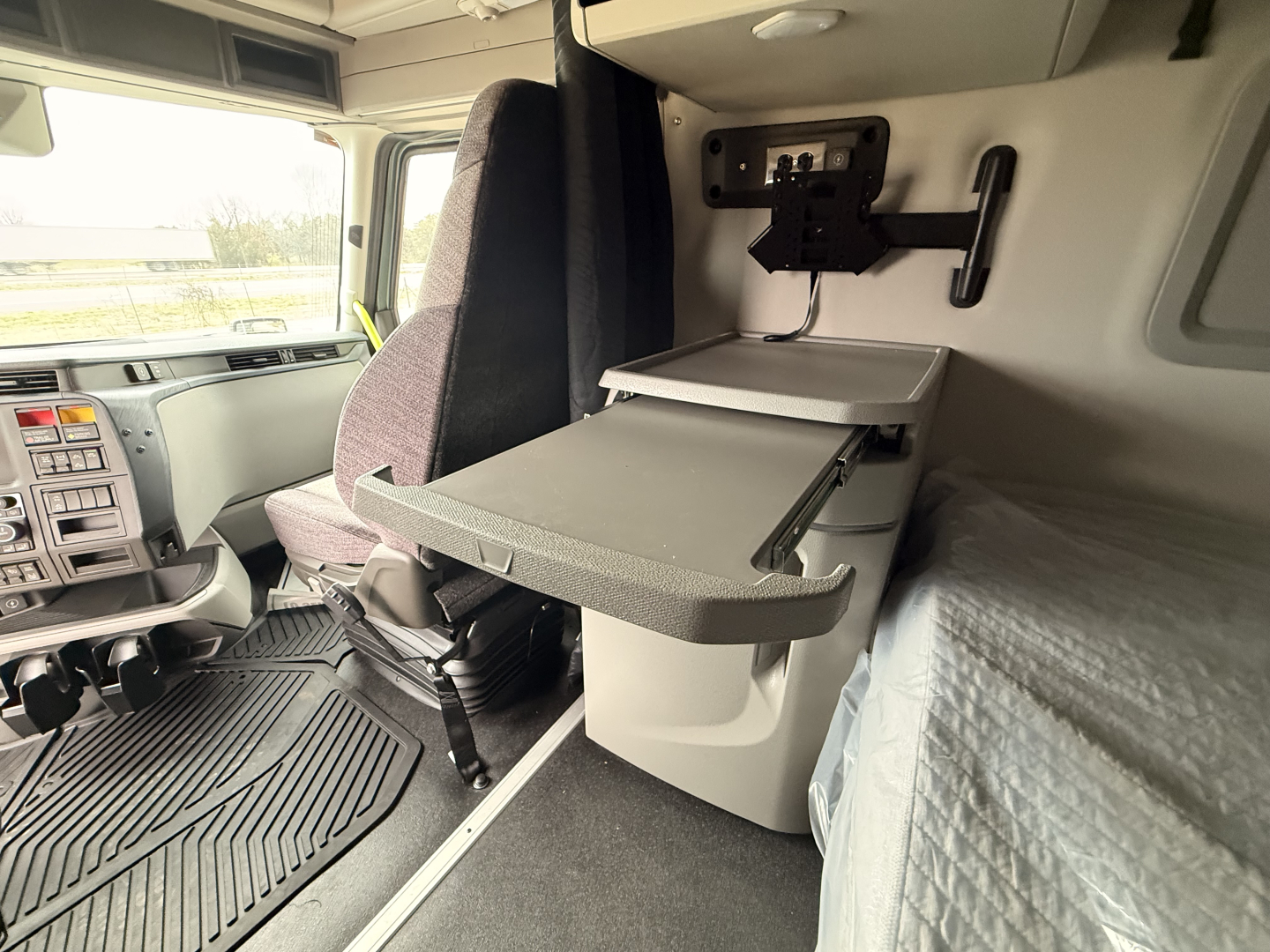 Volvo VNL cab interior showing a flip-down shelf/slide-out desk and sleeper area with bed, driver seat, dash controls visible.